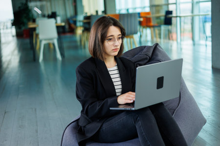 Smiling business woman, company employee, working holding laptop while sitting in modern office. Modern business woman working online.の写真素材