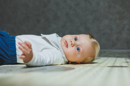 A blue-eyed baby is lying on the floor and holding his head. Development of the baby. A child in a...