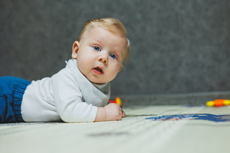 A blue-eyed baby is lying on the floor and holding his head. Development of the baby. A child in a white bodysuitの写真素材