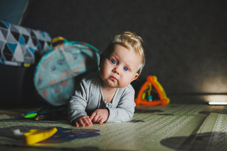 Cute blond toddler boy playing with baby toys at home sitting on carpet in living room. Smiling cute...