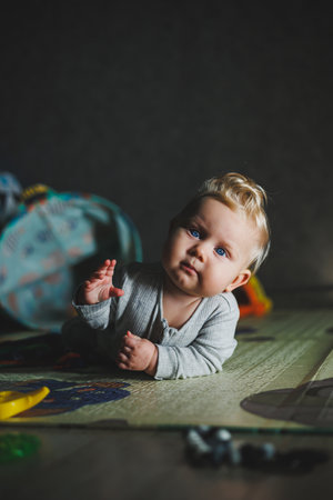 Cute blond toddler boy playing with baby toys at home sitting on carpet in living room. Smiling cute little child using colorful toys, chewing teetherの写真素材