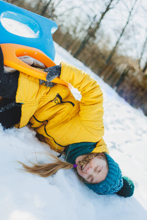 A cheerful girl in a yellow winter coat runs in the snow. A child plays with snowballs in winter....