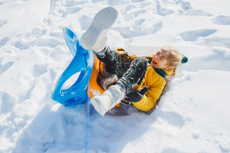 A cheerful girl rides a sled in the snow in winter. The child goes out on a sleigh. Winter entertainment for children.の写真素材