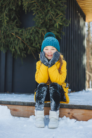 A cheerful girl in a yellow winter coat runs in the snow. A child plays with snowballs in winter....