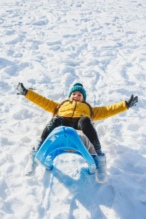 A cheerful girl in a yellow winter coat runs in the snow. A child plays with snowballs in winter....