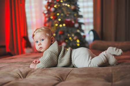 Cute baby boy on background with Christmas tree toys, traditional Christmas costume. New Year...