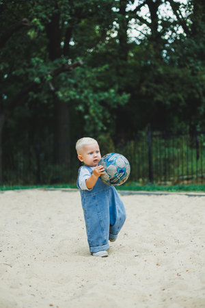 A 1-year-old boy plays with a soccer ball on the street. The child is playing in the fresh air. Stylish little blond boy.の写真素材