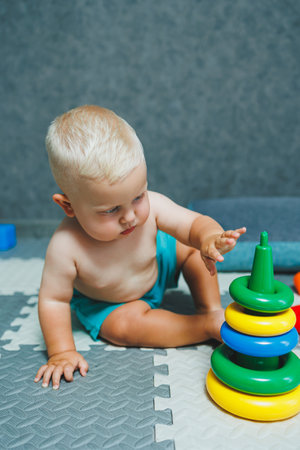 A little boy in shorts sits on the carpet at home and plays with educational toys. A child builds a plastic pyramid.の写真素材