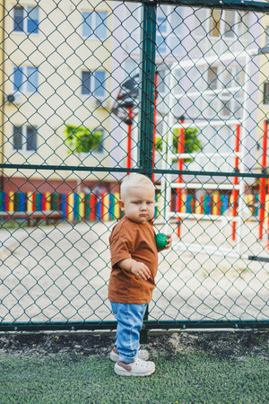 A 1-year-old boy in stylish jeans and a T-shirt is playing on the street. A child plays outdoors on a playground. A child on the football field.の写真素材