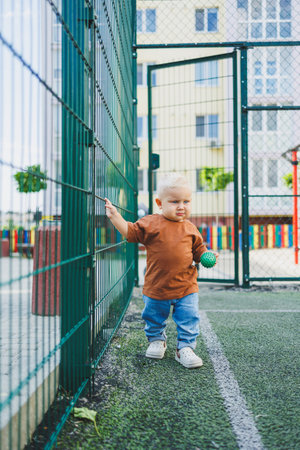 A 1-year-old boy in stylish jeans and a T-shirt is playing on the street. A child plays outdoors on a playground. A child on the football field.の写真素材