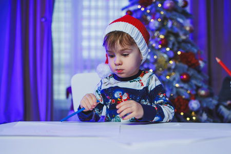 A little boy sits at home at the table and plays on the background of a Christmas tree. Christmas tree at home. A child's New Year's mood.の写真素材