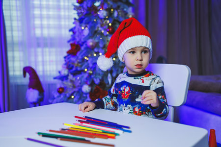 A little boy sits at home at the table and plays on the background of a Christmas tree. Christmas tree at home. A child's New Year's mood.の写真素材