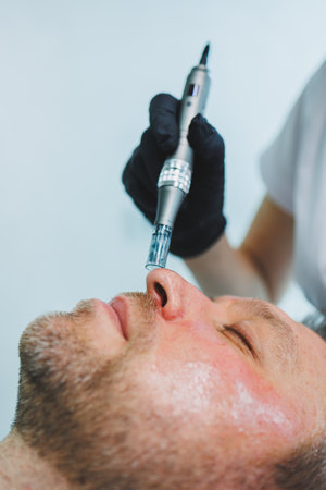 A beautician makes a mask on the face of a man with a beard. Male cosmetology. Preservation of youth and facial skin care. Beauty salon concept.の写真素材