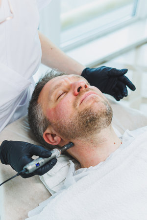 A beautician makes a mask on the face of a man with a beard. Male cosmetology. Preservation of youth and facial skin care. Beauty salon concept.の写真素材