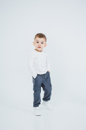 A boy in a white longsleeve and joggers on a white background. Cheerful boy in stylish clothes.の写真素材