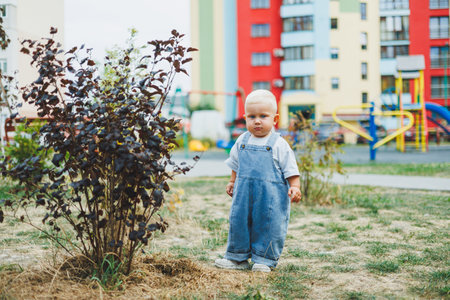A toddler boy in denim overalls runs and plays on the playground. Active time of the child outside....