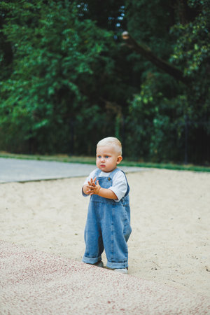 A toddler boy in denim overalls runs and plays on the playground. Active time of the child outside....