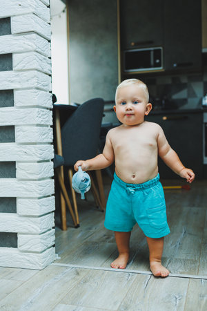 A toddler boy in shorts runs around the apartment at home. The child is playing at home. Active entertainment at home with the child.の写真素材