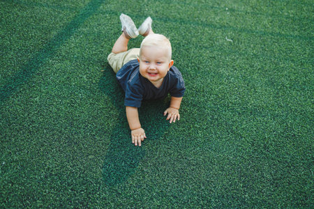 Cute toddler boy lying on green grass. Active time of the child outside. A child runs on the street...