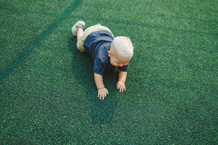 Cute toddler boy lying on green grass. Active time of the child outside. A child runs on the street in the summer.の写真素材