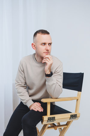 A young man sits on a chair and shows his emotions to the camera.