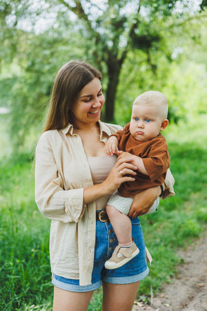 A young mother holds her little son in her arms and walks in the park. A walk of a mother with her son.の写真素材