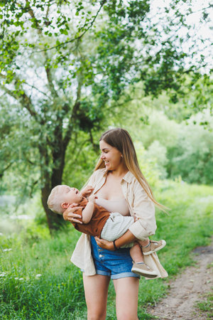 A young mother holds her little son in her arms and walks in the park. A walk of a mother with her son.の写真素材