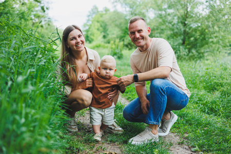 A family couple with a small son are standing in the park on the grass. Mother, father and child...