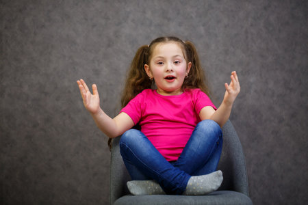 little girl in a pink t-shirt is sitting on a gray chair. Emotional photo of a childの写真素材