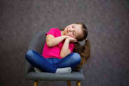 little girl in a pink t-shirt is sitting on a gray chair. Emotional photo of a childの写真素材
