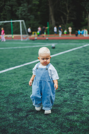 A one-year-old blond boy in a t-shirt and denim dungarees walks in the fresh air. Self-development of the child.の写真素材