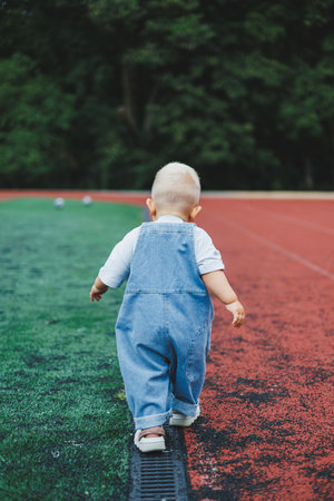 A one-year-old blond boy in a t-shirt and denim dungarees walks in the fresh air. Self-development of the child.の写真素材