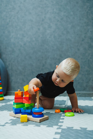 A toddler boy sits on a rug and plays with a wooden pyramid. Development of the baby. Toys for babiesの写真素材