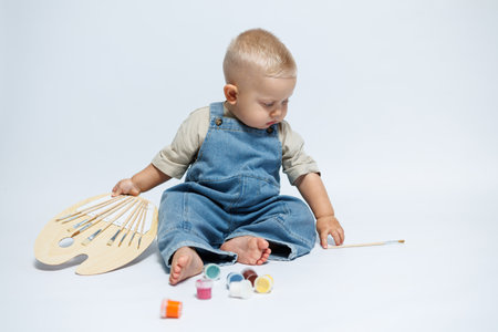 Boy 1 year old draws with paints sitting on a white background. Child is a little artist. Child...