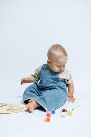 Boy 1 year old draws with paints sitting on a white background. Child is a little artist. Child...