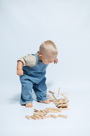 Cute boy in denim dungarees on a white background. Child playing with wooden toys. Smiling toddler in a great moodの写真素材