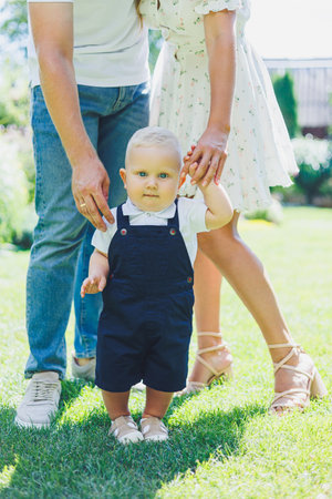 Little boy learning to walk holding hands with mom and dad. Child taking first steps.