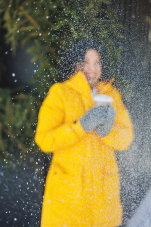 A smiling woman in a bright yellow down jacket with coffee in her hands is enjoying the snow. A walk on a snowy day. Takeaway coffee in a paper cup.の写真素材