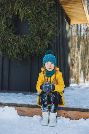A cheerful girl in a yellow winter coat runs in the snow. A child plays with snowballs in winter. Children's winter entertainment.の写真素材