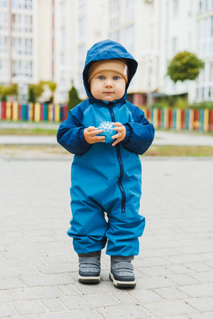 A little boy in overalls runs on the street. A child in a raincoat walks in the yard. Children's...
