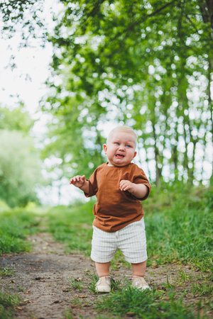 Little boy 1 year old takes his first steps outside. Child learns to walk.の写真素材