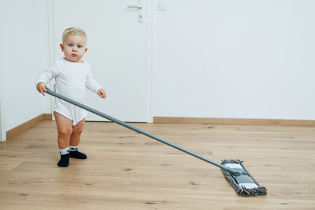 Little boy washes the floor with a mop. Toddler cleans at home. Mop for cleaning in the apartment.の写真素材