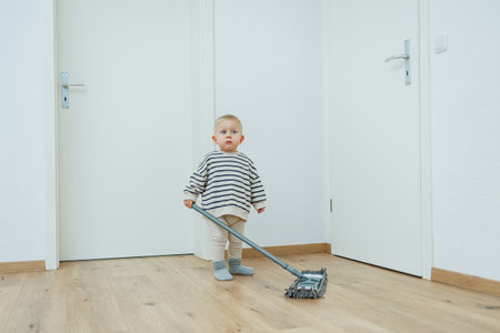 Toddler boy washes the floor with a mop, helping his mother clean the house. The child learns to clean the house.の写真素材
