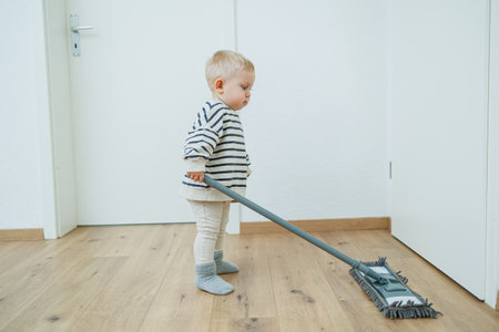 Child boy cleaning the floor at home. Boy washes the floor with a mop for cleaning in the apartment. Children are happy to help with cleaning the house.の写真素材