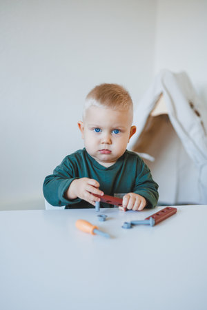 Toddler boy in a bright room sits at a children's table and plays with toys. Furniture for children. Table and chairs for babies. Child developmentの写真素材