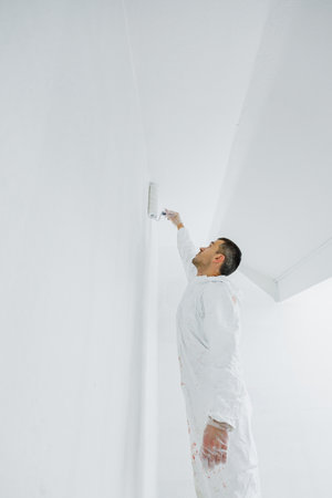 A man in a white uniform with a roller in his hand paints the ceiling white at home. Renovation of premises.の写真素材