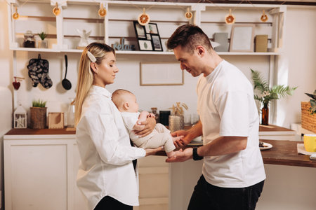 Happy family with newborn son playing in the kitchen. Family couple at home with son in the kitchen....