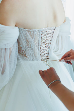 A closeup of a brides stunning dress being laced, highlighting its intricate design and sheer...