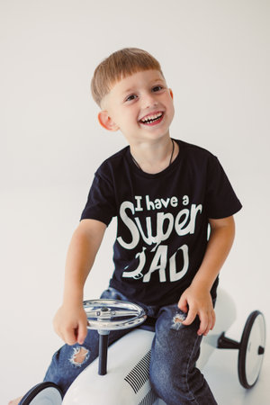 A cheerful boy dressed in a black shirt joyfully declares while happily sitting on a toy vehicleの写真素材
