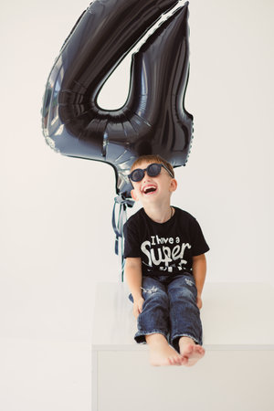 A joyful child in sunglasses poses happily next to a large, colorful balloon shaped like the number...